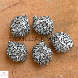 May include: Five silver and white diamond cage beads. The beads are made of silver and are set with small, white diamonds. The diamonds are set in a cage-like design, and the beads are all the same size and shape.