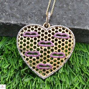 May include: A gold heart-shaped pendant necklace with a delicate diamond-encrusted border. The pendant features a mesh design with pink lips outlined in small pink gemstones.