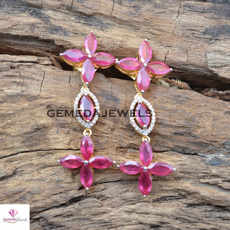 May include: A pair of dangle earrings with a gold setting and pink gemstones. The earrings feature a flower design with a teardrop-shaped pendant.