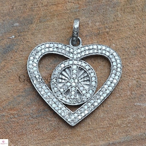 May include: A silver heart-shaped pendant with a peace sign in the center, both covered in small, clear diamonds.