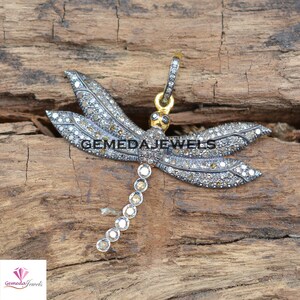 Peut inclure: Un pendentif en argent en forme de libellule avec une cha&icirc;ne en or et des diamants clairs et bruns. Le pendentif est plac&eacute; sur un fond en bois.