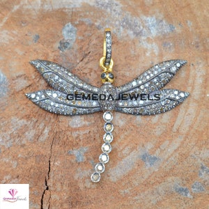 Peut inclure: Un pendentif en argent en forme de libellule avec un corps dor&eacute; et des diamants clairs et bruns. Les ailes de la libellule sont recouvertes de petits diamants. Le pendentif est sur une surface en bois brun.