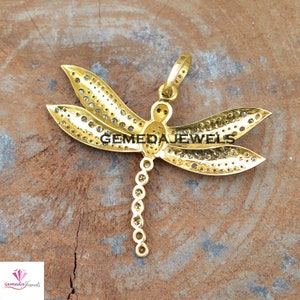 Peut inclure: Pendentif en forme de libellule en or avec des pierres transparentes. Les ailes de la libellule sont recouvertes de petites pierres et le corps est une seule pierre. Le pendentif a une boucle en haut pour l'attacher &agrave; une cha&icirc;ne.