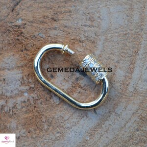 Puede incluir: Cierre de metal dorado con un barril cil&iacute;ndrico incrustado de diamantes. El cierre est&aacute; abierto y el barril es visible. El texto "GEMEDAJEWELS" es visible en la imagen.