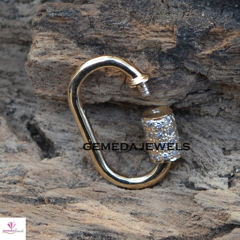 Puede incluir: Cierre de metal dorado con un dije cil&iacute;ndrico incrustado con peque&ntilde;as piedras transparentes. El dije est&aacute; grabado con el texto "GEMEDAJEWELS".