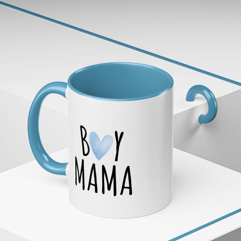 Puede incluir: Taza de cer&aacute;mica blanca con borde y asa azules. La taza tiene un coraz&oacute;n azul de acuarela y el texto "Boy Mama" en negro.