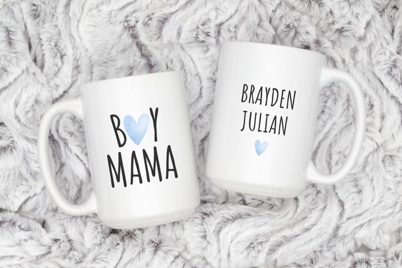 Puede incluir: Dos tazas de cer&aacute;mica blanca con texto negro y corazones azules. Una taza dice "Boy Mama" y la otra dice "Brayden Julian".