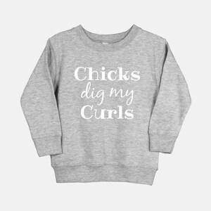 Puede incluir: Una sudadera gris con el texto "Chicks dig my Curls" impreso en blanco.
