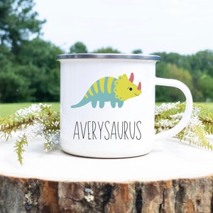 K&ouml;nnte beinhalten: Wei&szlig;er Emaillebecher mit silbernem Rand und wei&szlig;em Henkel. Der Becher zeigt einen Cartoon-Triceratops in Blau und Gelb mit dem Namen "Averysaurus" darunter in Schwarz.