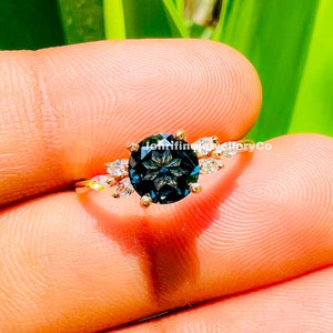 May include: A gold ring with a large, dark blue gemstone surrounded by smaller, clear gemstones. The ring is set in a delicate, floral design.
