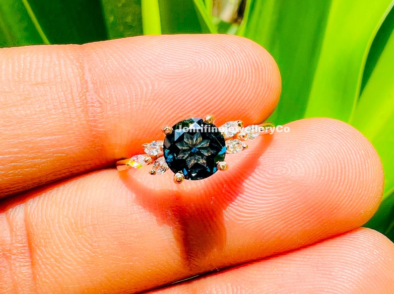 May include: A gold ring with a large, dark blue gemstone surrounded by smaller, clear gemstones. The ring is set in a delicate, floral design.
