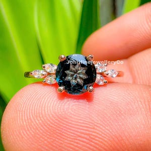 May include: A ring with a large, dark blue gemstone surrounded by smaller, clear gemstones. The ring is set in a silver band and has a delicate, floral design.