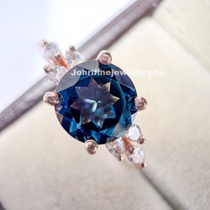 May include: A rose gold ring with a large, dark blue gemstone surrounded by smaller, clear gemstones. The ring is set in a delicate, floral design.