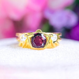 May include: A gold ring with a large, dark purple gemstone surrounded by smaller, clear gemstones.