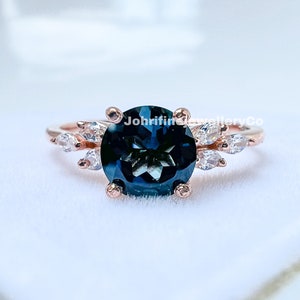 May include: A rose gold ring with a large, round, dark blue gemstone surrounded by smaller, clear gemstones. The ring is set in a delicate, floral design.