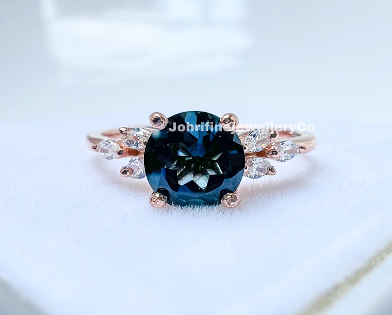 May include: A rose gold ring with a large, round, dark blue gemstone surrounded by smaller, clear gemstones. The ring is set in a delicate, floral design.