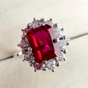 Può includere: Un anello d'argento con una grande gemma rossa rettangolare al centro, circondata da un alone di gemme chiare più piccole. Il design dell'anello è elegante e accattivante, adatto per occasioni speciali.