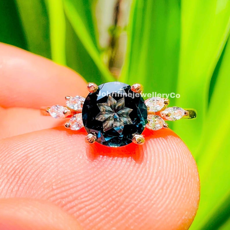 May include: A gold ring with a large, round, dark blue gemstone with a star-shaped pattern. The gemstone is surrounded by smaller, round, white gemstones.