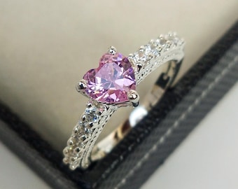May include: A silver ring with a pink heart-shaped gemstone and a row of smaller clear gemstones around the band.