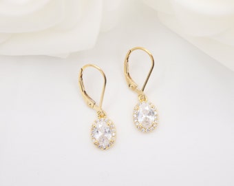 May include: A pair of gold earrings with oval-shaped clear stones surrounded by smaller clear stones. The earrings have a lever back closure.
