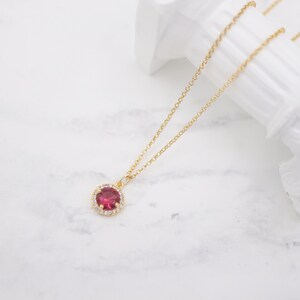 May include: A gold chain necklace with a pendant featuring a red gemstone surrounded by a halo of smaller clear gemstones.