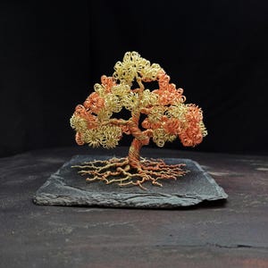 May include: A wire sculpture of a tree with a copper and gold finish. The tree is on a black slate base.