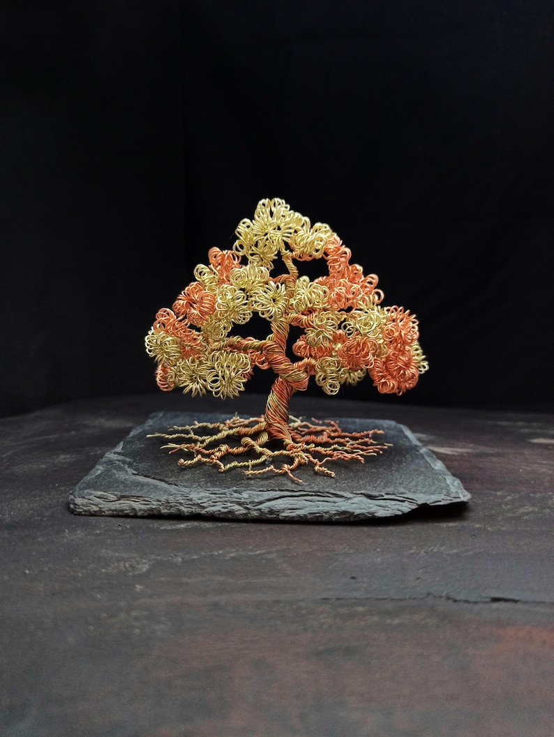 May include: A wire sculpture of a tree with a copper and gold finish. The tree is on a black slate base.