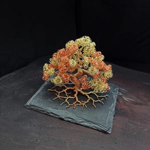 May include: A wire sculpture of a tree with a copper and gold finish. The tree is on a black slate base.