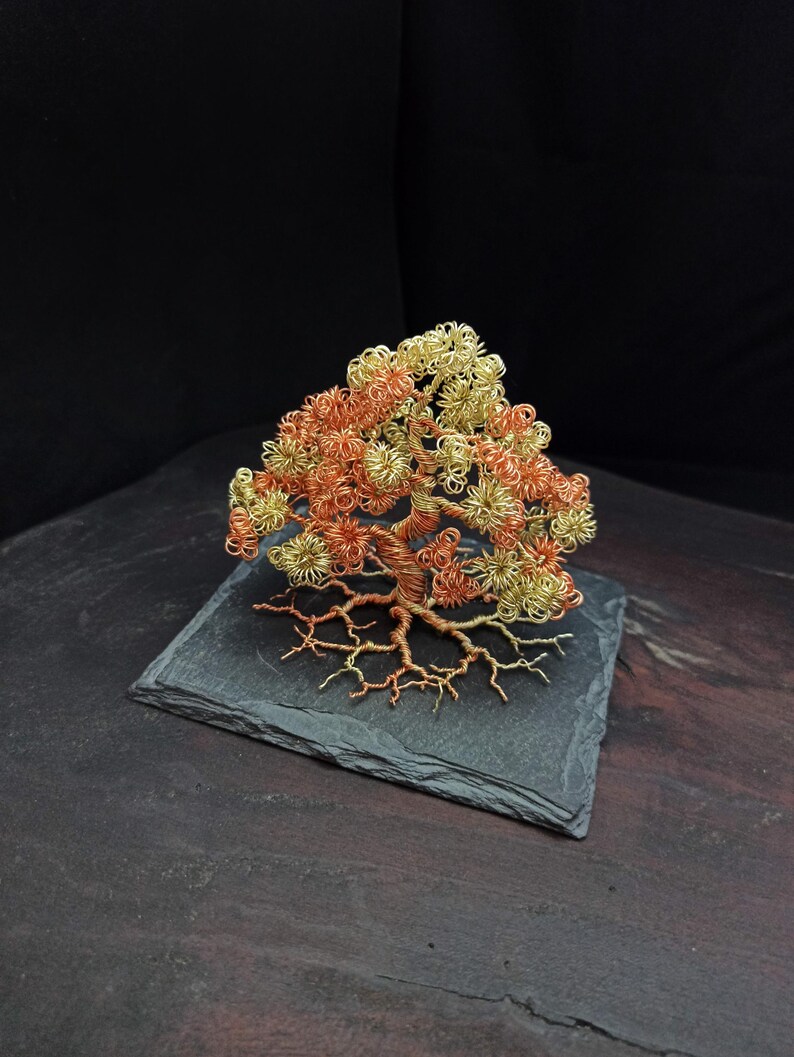 May include: A wire sculpture of a tree with a copper and gold finish. The tree is on a black slate base.