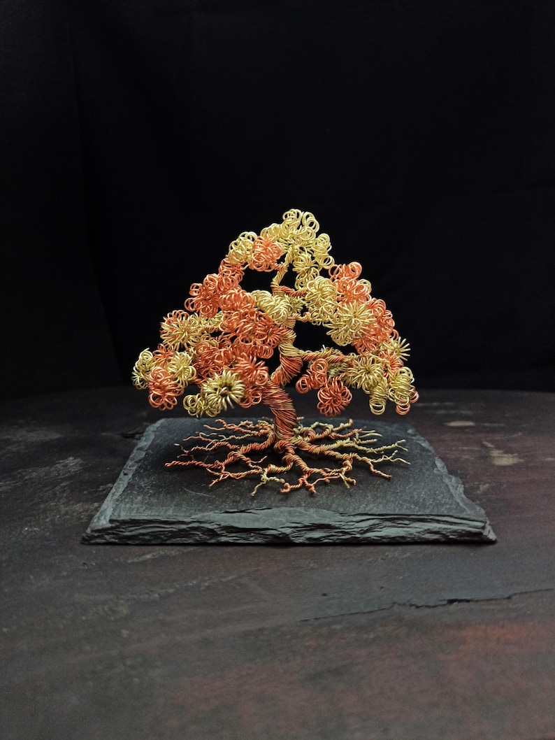 May include: A wire sculpture of a tree with a copper trunk and gold leaves. The tree is sitting on a black slate base.