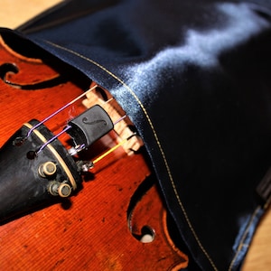 May include: A close-up of a violin with a black and gold scroll and a black sound post. The violin is partially covered by a dark blue velvet case.