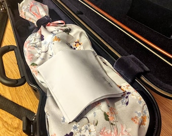 May include: Black violin case with a floral patterned fabric lining. The case is open and a bow is inside. The case has a strap and a label that says "bam".