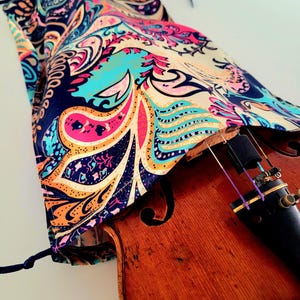 Könnte beinhalten: Ein Geigenkoffer mit Paisley-Muster und Kordelzug, der eine hölzerne Geige bedeckt.