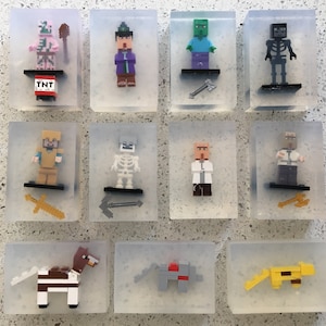 May include: Twelve clear plastic boxes each containing a different Minecraft character figurine. The characters include a pig, a wizard, a zombie, a skeleton, a knight, a skeleton, a scientist, a villager, a horse, a wolf, and a cat.