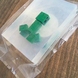 May include: A clear plastic mold with a green Minecraft Creeper character inside.