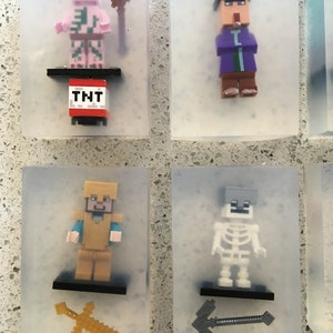 May include: Six clear plastic squares with Minecraft character figurines inside. The characters include a pink pig-like creature with a pickaxe, a purple-robed wizard with a staff, a golden-armored warrior with a sword, a skeleton with a pickaxe, a creeper with a TNT block, and a villager with a sword.