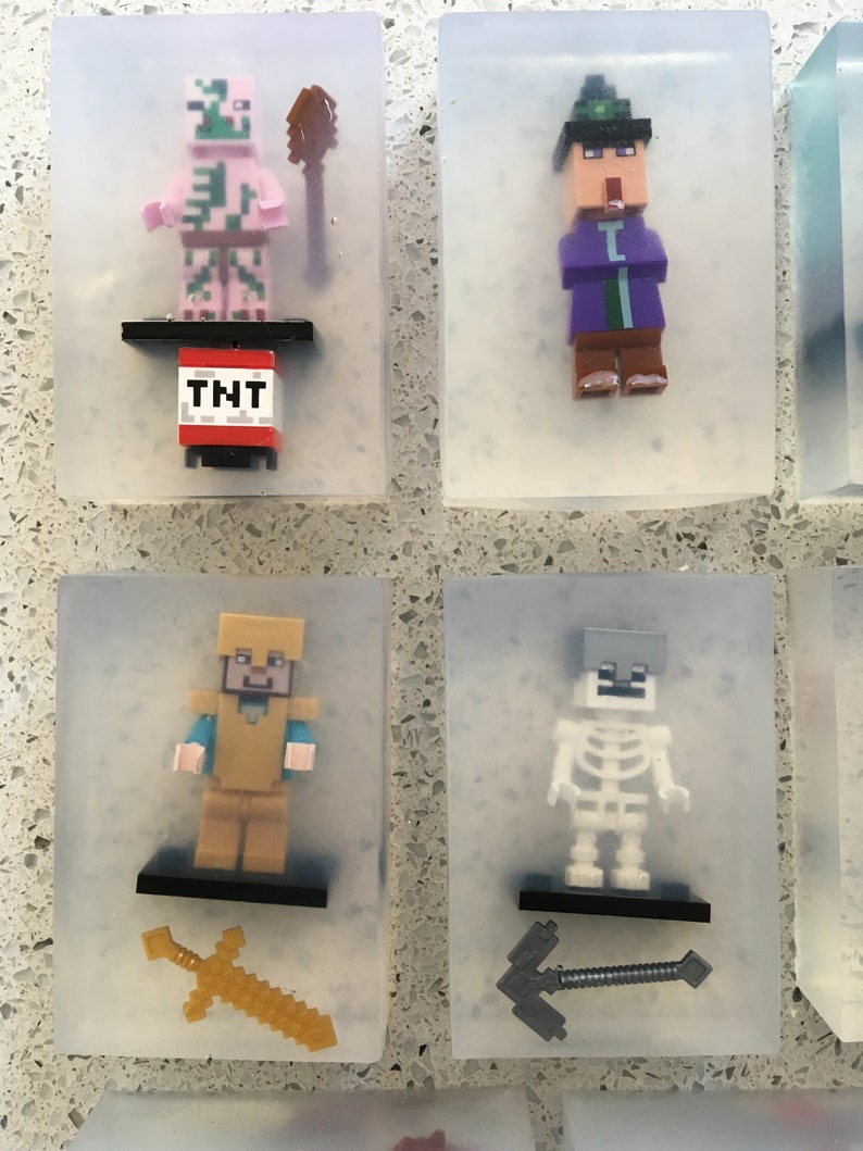 May include: Six clear plastic squares with Minecraft character figurines inside. The characters include a pink pig-like creature with a pickaxe, a purple-robed wizard with a staff, a golden-armored warrior with a sword, a skeleton with a pickaxe, a creeper with a TNT block, and a villager with a sword.