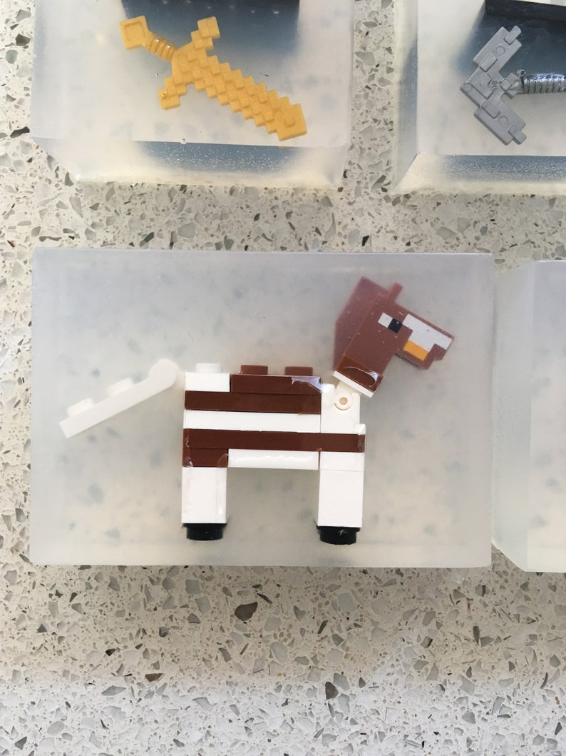 May include: A white and brown Lego horse figurine with a brown head and tail. The horse is standing on a clear plastic base.