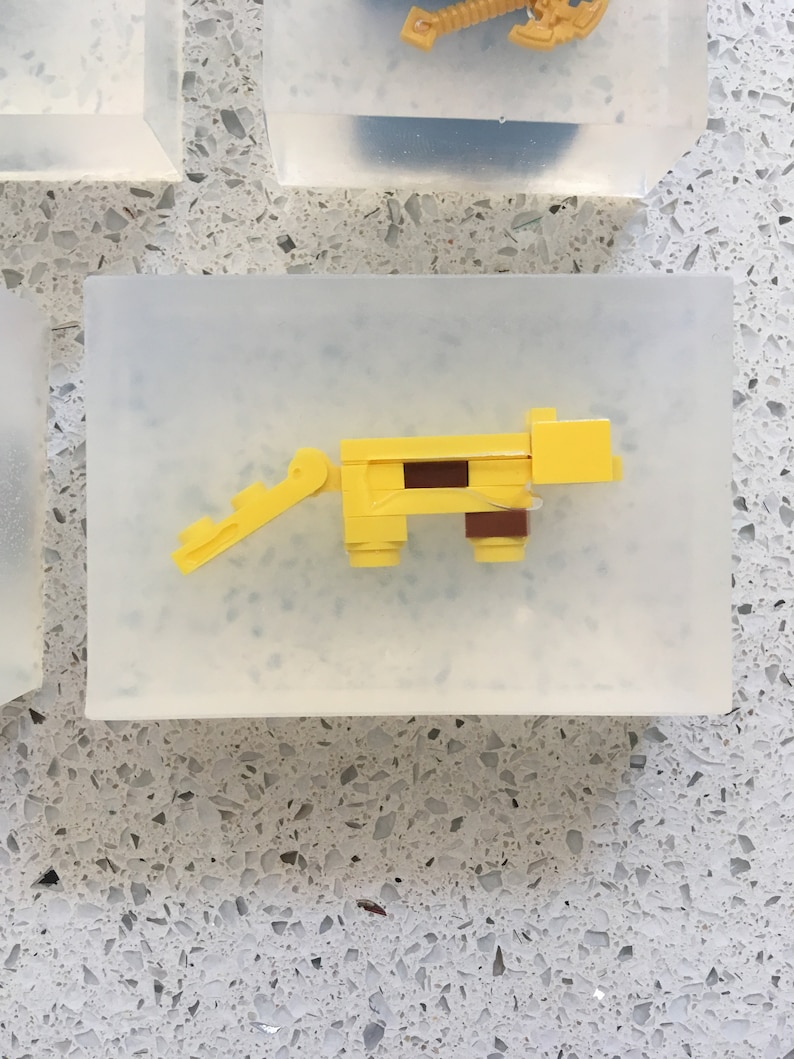 May include: A yellow plastic toy animal with a brown stripe on its back. The toy is made of Lego bricks and is sitting on a clear surface.