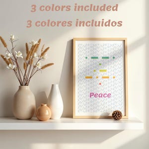 Puede incluir: Una impresión enmarcada con un marco de madera clara muestra un diseño de código Morse colorido con la palabra "Peace" en rosa. La imagen está sobre una estantería blanca con jarrones y una piña decorativa.