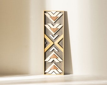 Op de afbeelding: Een houten wandkunstwerk met een geometrisch ontwerp met een reeks overlappende driehoeken in tinten bruin, wit en grijs. Het stuk is ingelijst in een natuurlijke houten lijst.