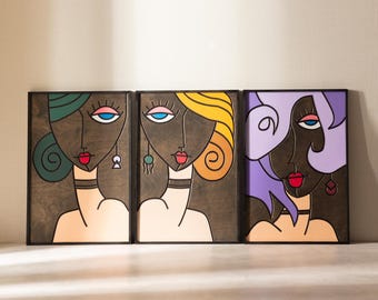 May include: Three framed wood wall art pieces with abstract portraits of women with colorful hair and bold features. The portraits are painted in a modern style with black outlines and bright colors.