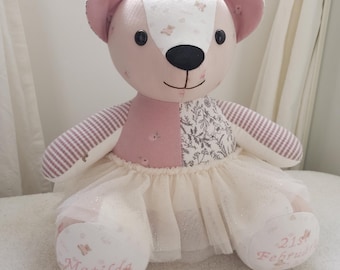 May include: A stuffed bear toy made of patchwork fabric in shades of pink, white, and grey with floral and striped patterns. The bear wears a cream-coloured tulle skirt. The left foot is embroidered with the name Matilda and the right with 21st February.