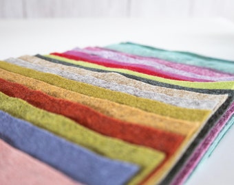 Könnte beinhalten: Ein Stapel bunter Filzquadrate in verschiedenen Farbtönen, darunter Rosa, Blau, Grün, Orange und Rot. Die Filzquadrate sind ordentlich angeordnet und erzeugen eine ansprechende Darstellung von Texturen und Farben. Das Bild ist gut beleuchtet.