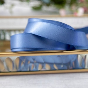 K&ouml;nnte beinhalten: Ein blaues Satinband ist auf einem goldgerahmten Glastablett mit einem dekorativen Muster aufgerollt und ausgestellt.