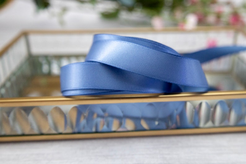 K&ouml;nnte beinhalten: Ein blaues Satinband ist auf einem goldgerahmten Glastablett mit einem dekorativen Muster aufgerollt und ausgestellt.