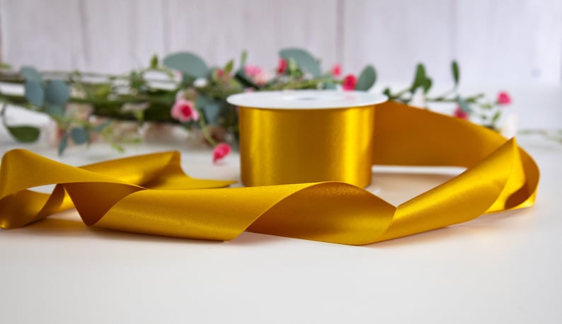 K&ouml;nnte beinhalten: Eine Spule mit goldenem Satinband, auf der ein St&uuml;ck Band aufgewickelt ist. Das Band ist glatt und gl&auml;nzend.
