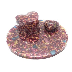 May include: A heart-shaped trinket box and a smaller heart-shaped trinket are both made of resin and embedded with dried rose petals. The trinkets are sitting on a larger, round resin tray also embedded with dried rose petals.