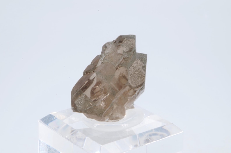 May include: A clear, smoky quartz crystal cluster with multiple facets. The crystal is displayed on a clear acrylic stand.