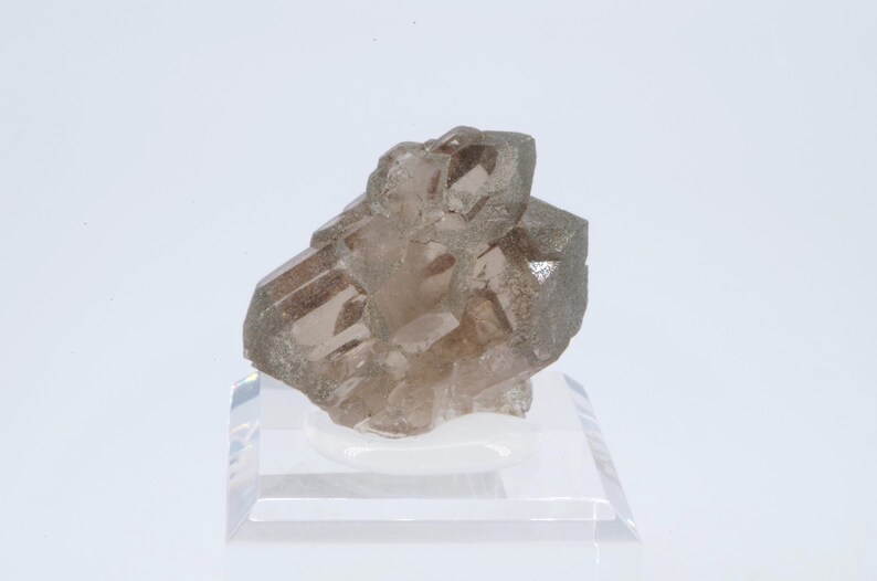 May include: A cluster of smoky quartz crystals on a clear acrylic display stand. The crystals are a light brown color and have a translucent appearance.